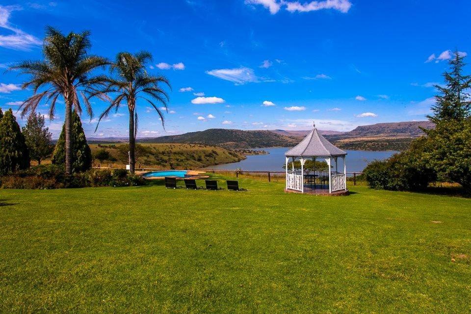 un cenador en un campo con un lago y palmeras en Blue Haze Country Lodge, en Estcourt