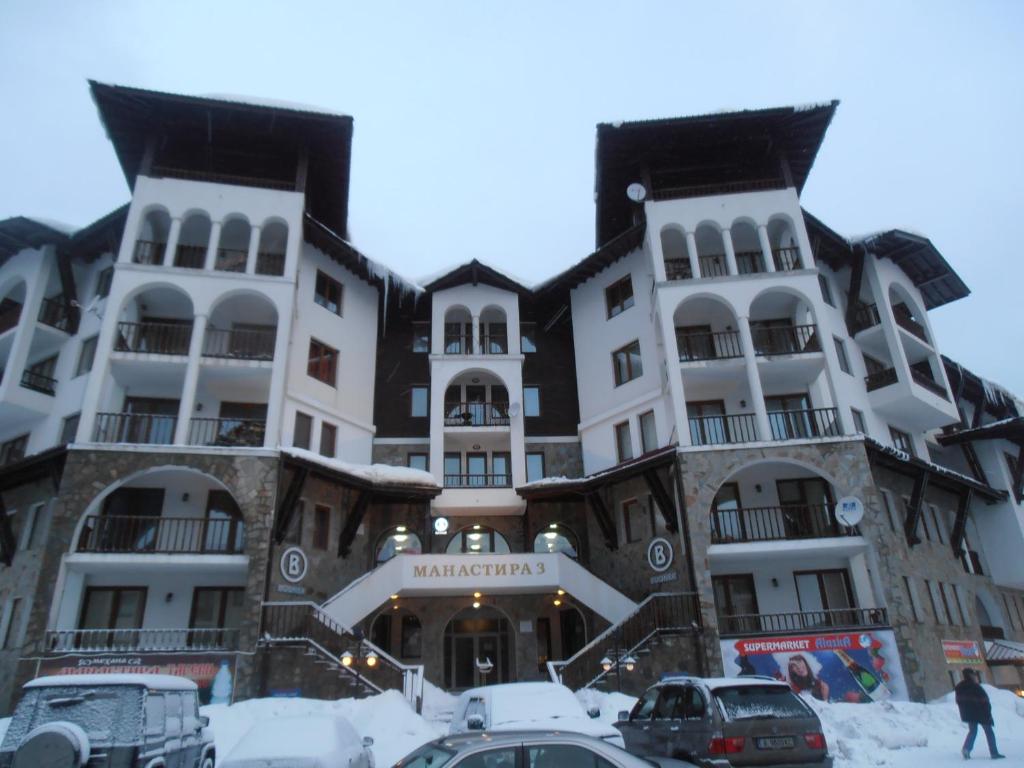 un edificio en la nieve con coches aparcados delante en Monastery 3 Apartments TMF, en Pamporovo