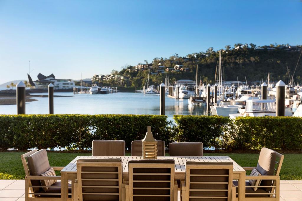 a wooden table and chairs with a view of a marina at Pavillion 17 - Waterfront Spacious 4 Bedroom With Own Inground Pool And Golf Buggy in Hamilton Island