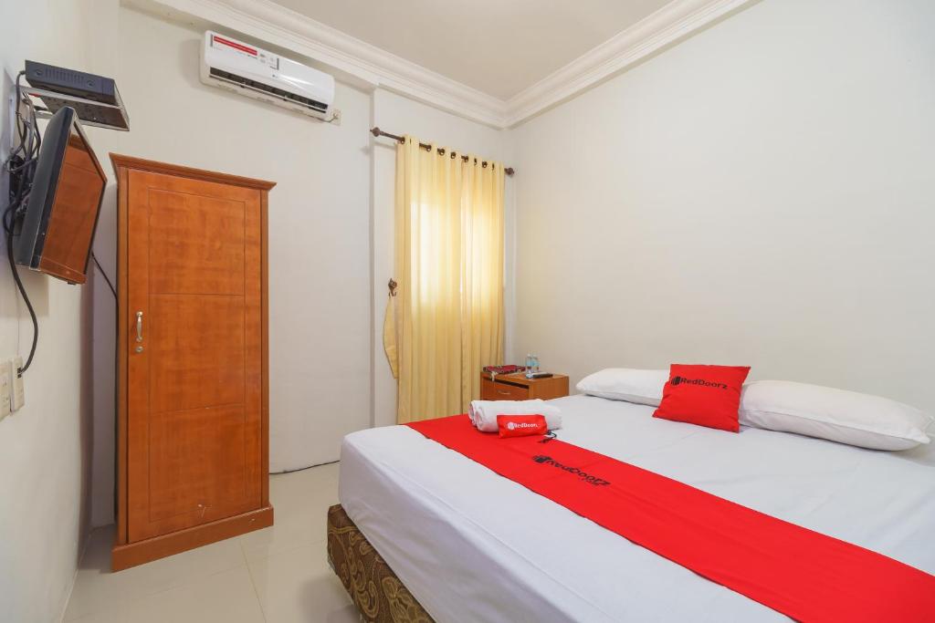 1 dormitorio con 1 cama blanca grande con detalles en rojo en RedDoorz Syariah @ Panglima Nyak Makam Aceh en Banda Aceh