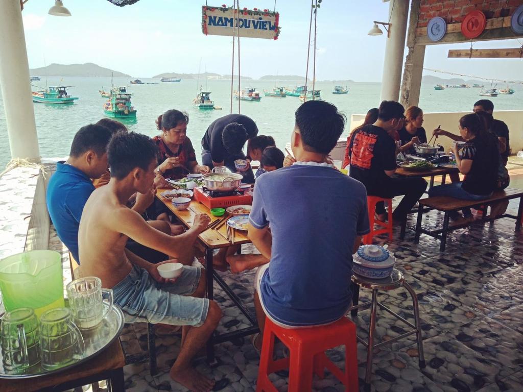 a group of people sitting at tables near the water at Nam Du VIEW Guest House in Nam Du