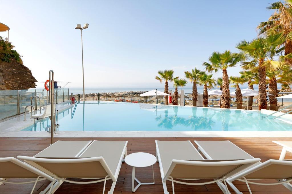 a pool at a resort with chairs and palm trees at Hotel Benalma Costa del Sol in Benalmádena