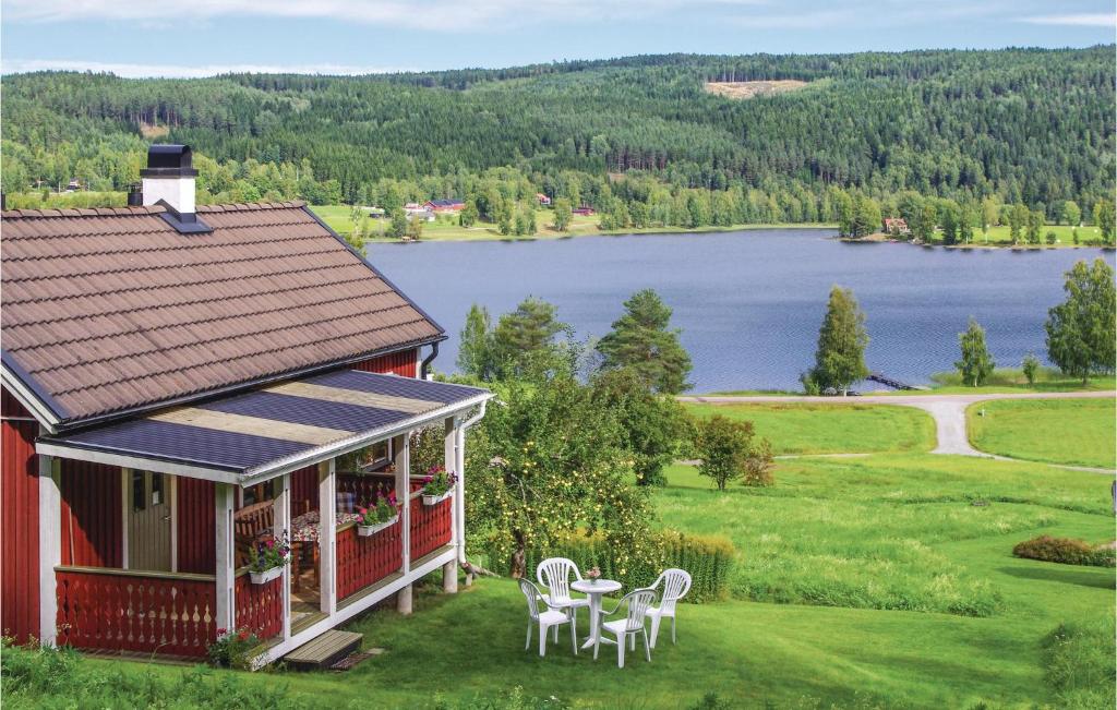 a red house with a table and chairs and a lake at Holiday Home Bosebyn Nordfalla Gunnarskog in Gunnarskog