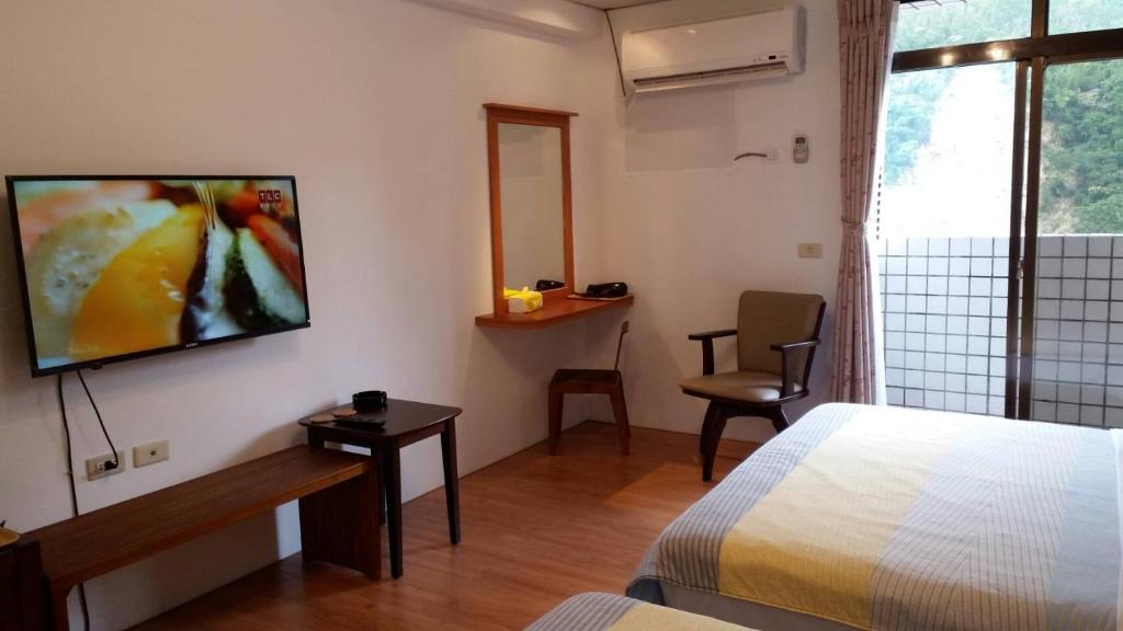 a hotel room with a bed and a television on the wall at Zhiben Hot Spring Hsiao Hotel in Wenquan