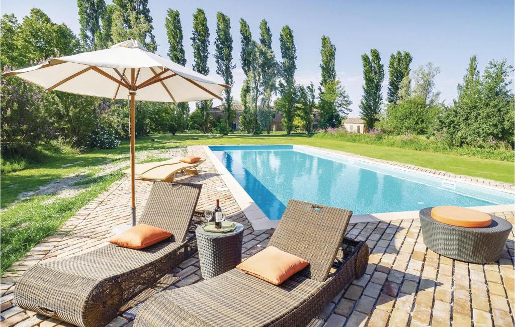 un patio con 2 sillas y una sombrilla junto a la piscina en Stunning Home In Taglio Di Po Ro With 2 Bedrooms, Wifi And Outdoor Swimming Pool, en Porto Viro