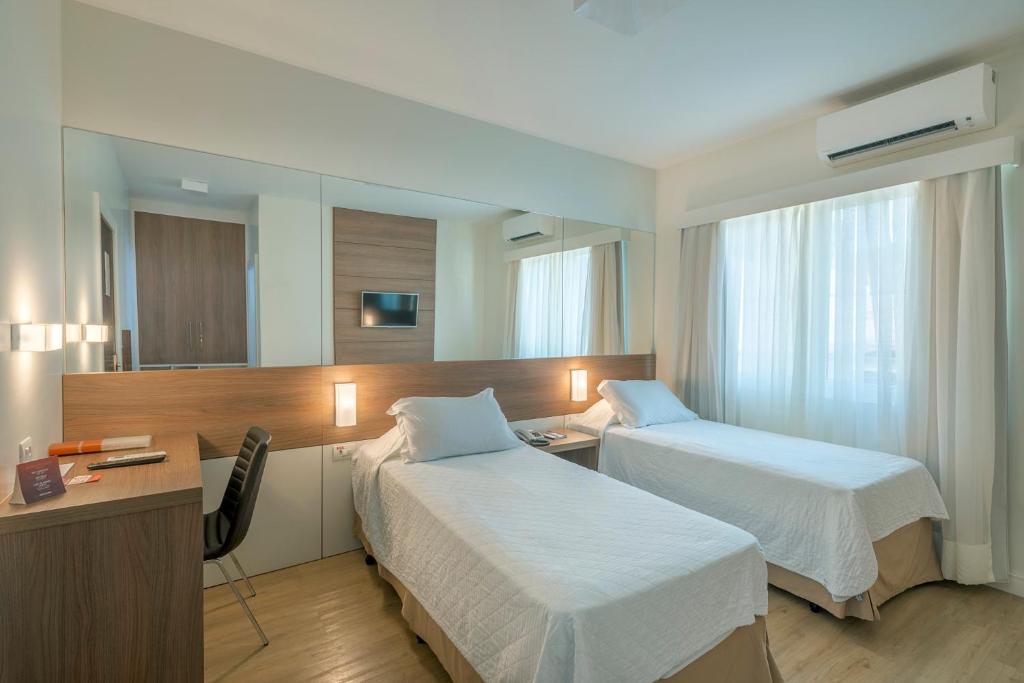 a hotel room with two beds and a desk at Hotel Glória Blumenau in Blumenau