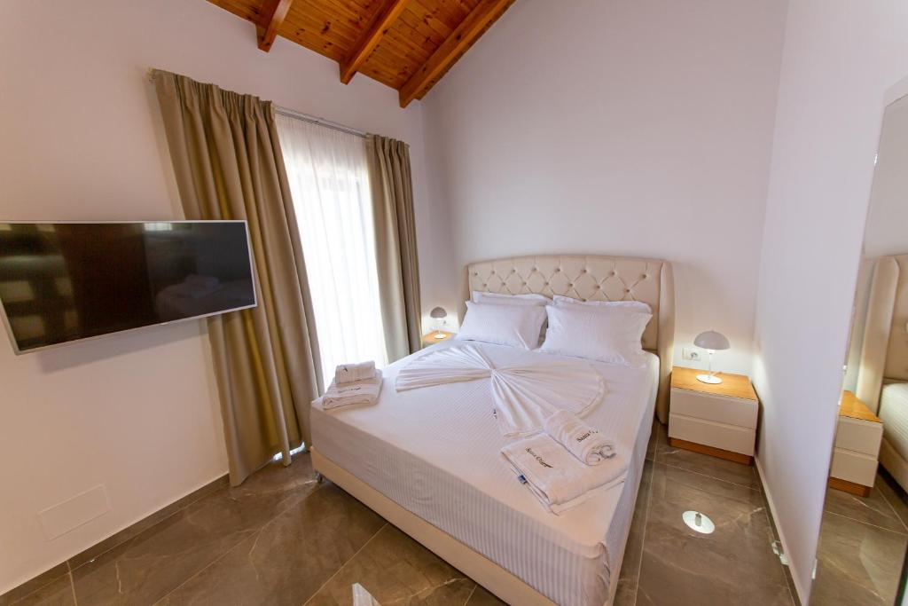 a bedroom with a bed with white sheets and a flat screen tv at Santa Oliva Suites in Ksamil
