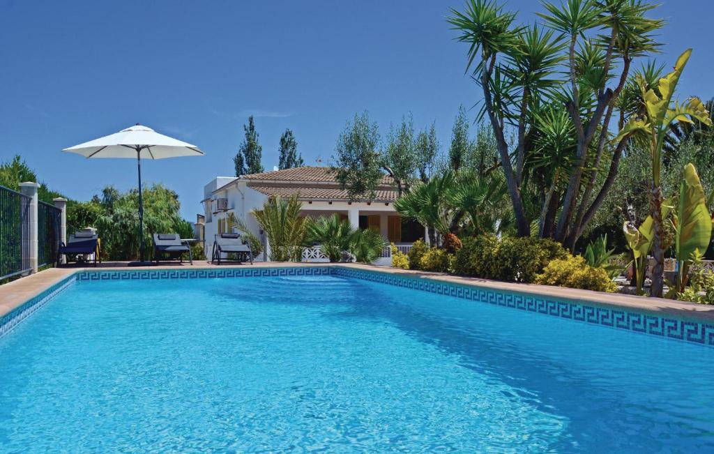 a blue swimming pool with an umbrella in front of a house at Lovely Home In Alcúdia in Alcudia