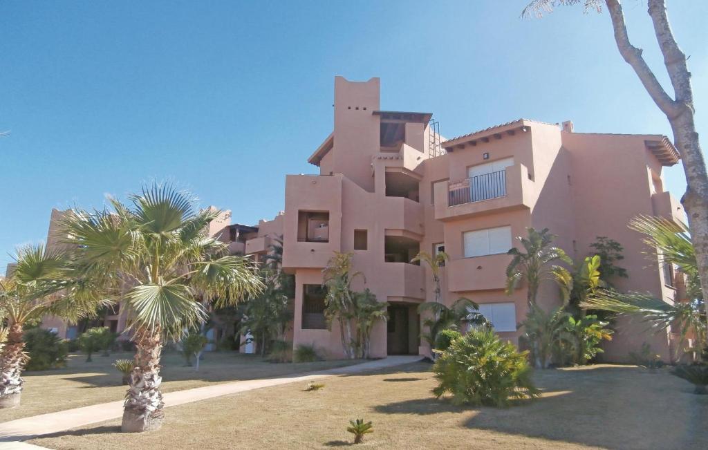 a large pink building with palm trees in front of it at Beautiful Apartment In Torre-pacheco With Outdoor Swimming Pool in Los Martínez