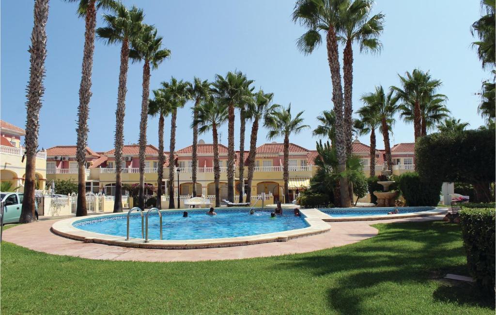a pool with palm trees in front of a building at Stunning Home In Orihuela Costa With 2 Bedrooms And Outdoor Swimming Pool in Playas de Orihuela