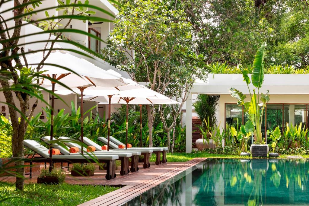 a pool with chairs and umbrellas next to a building at FCC Angkor by Avani in Siem Reap