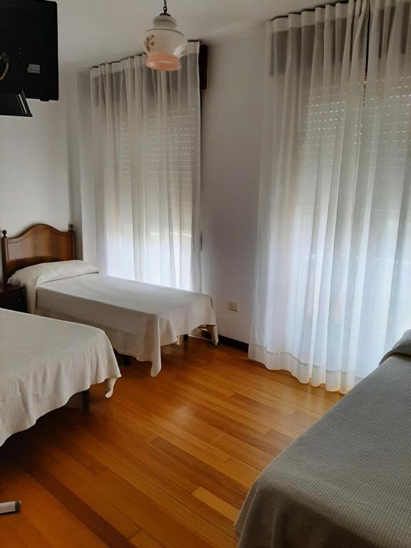 ビーゴにあるPensión Vista Alegreの白いカーテンとウッドフロアの客室で、ベッド2台が備わります。