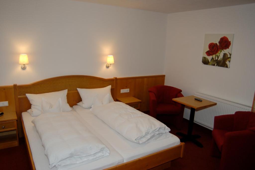 a bedroom with a bed with white sheets and a red chair at Landhotel Aschenbrenner in Freudenberg
