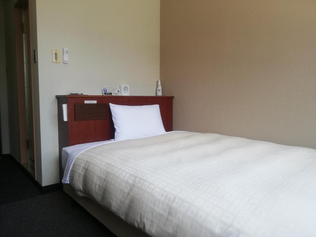 周南市にあるホテル徳山ヒルズ平和通り店のベッドルーム1室(大型ベッド1台、白いベッドシーツ付)