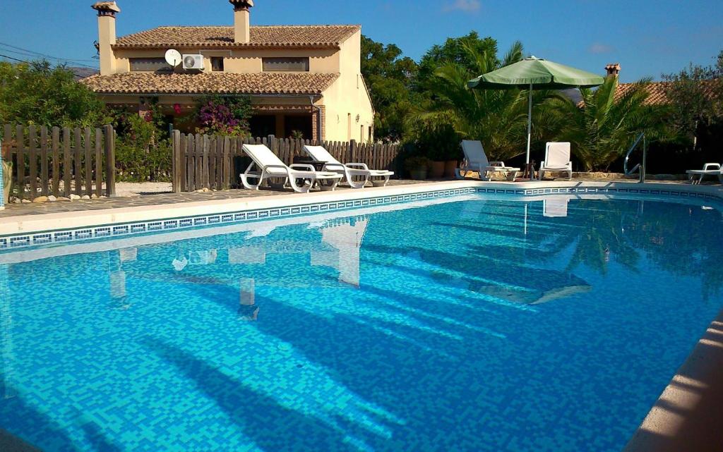 une grande piscine bleue avec des chaises et une maison dans l'établissement Finca El Corral, à Lliber