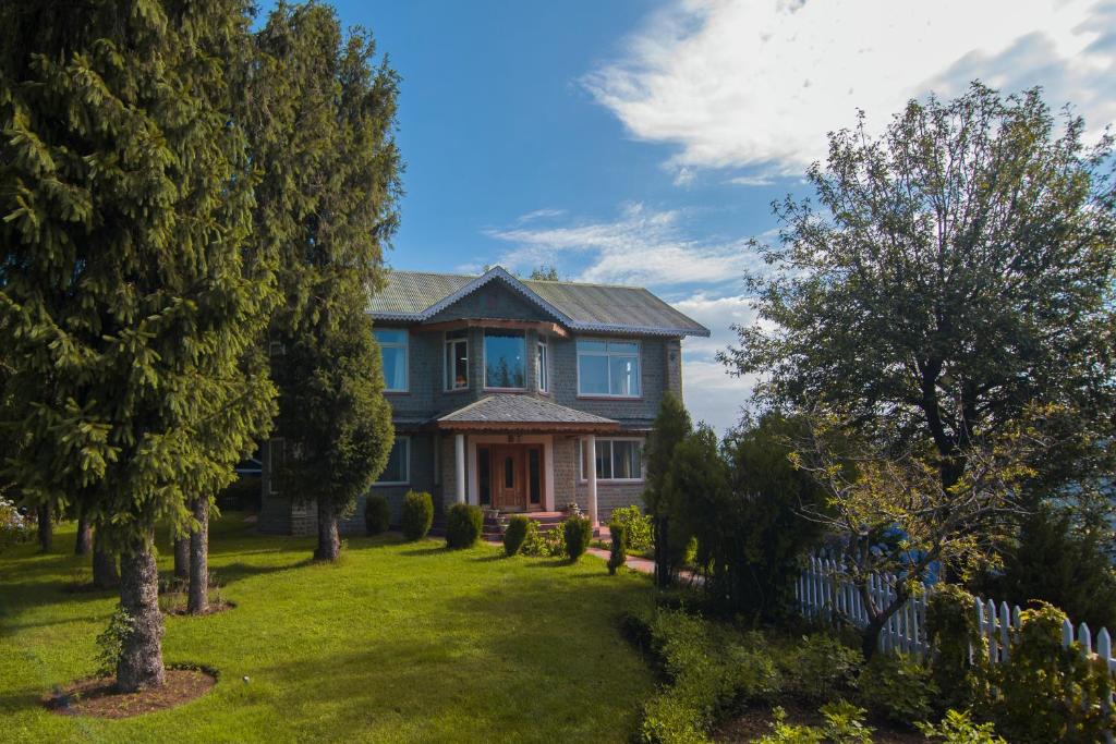 ein blaues Haus mit Bäumen und einem Zaun in der Unterkunft StayVista at Majestic Mountain View Villa in Dalhousie