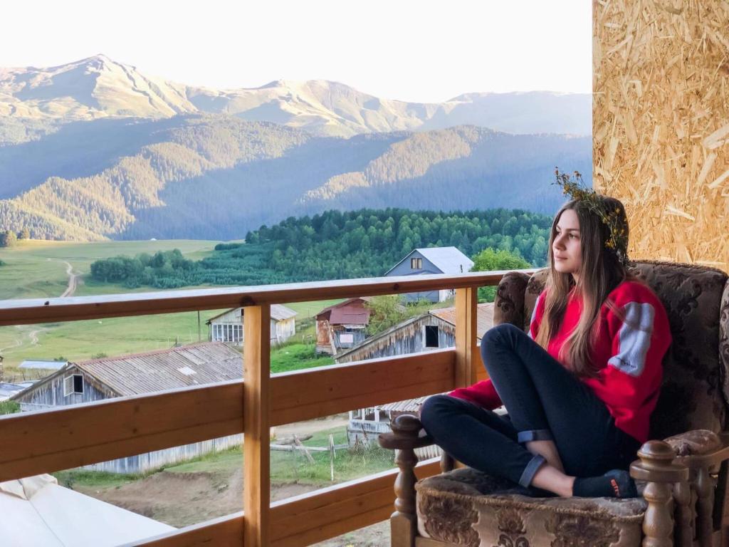 kobieta siedząca na krześle na balkonie z górami w obiekcie Tishe w mieście Omalo