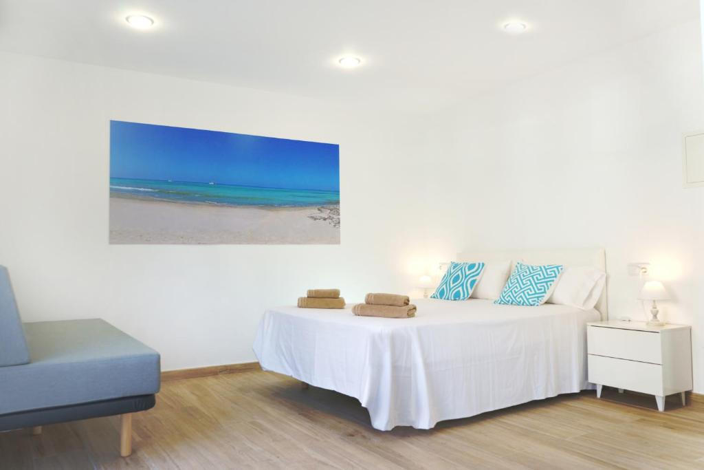 a white bedroom with a bed and a blue chair at Apartamentos Vistalmar Mallorca in Cala Figuera