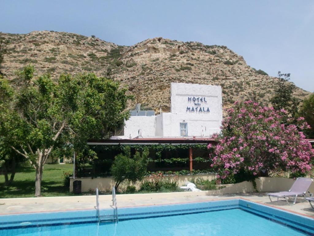 a hotel with a swimming pool in front of a mountain at Hotel Neos Matala in Matala