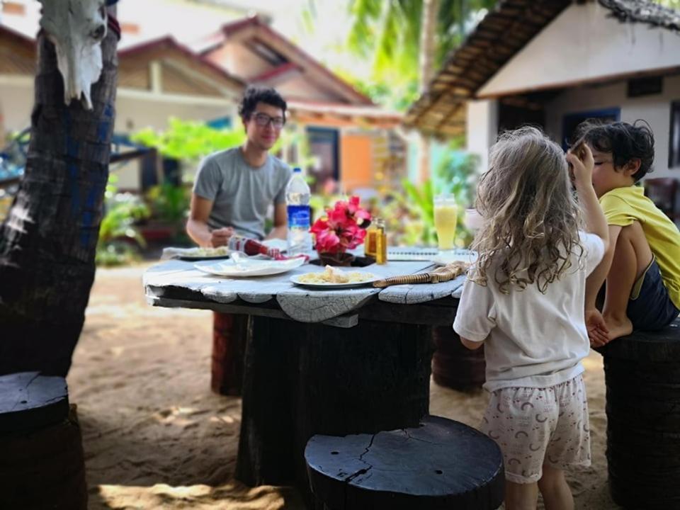 Um homem e duas crianças à volta de uma mesa com comida. em Star Rest Surf Camp Arugambay em Arugam Bay