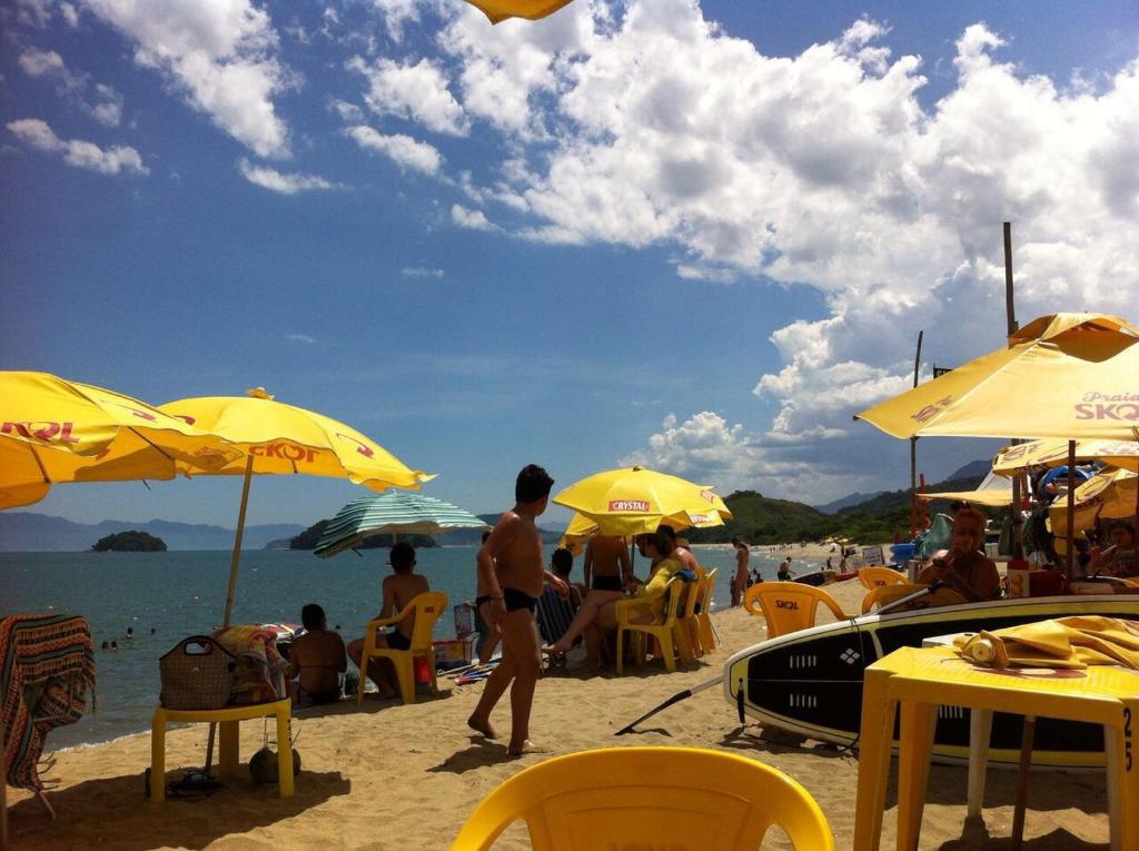 eine Gruppe von Menschen, die am Strand mit Sonnenschirmen sitzen in der Unterkunft Condomínio Mar Verde Caraguatatuba - CASA 55 in Caraguatatuba