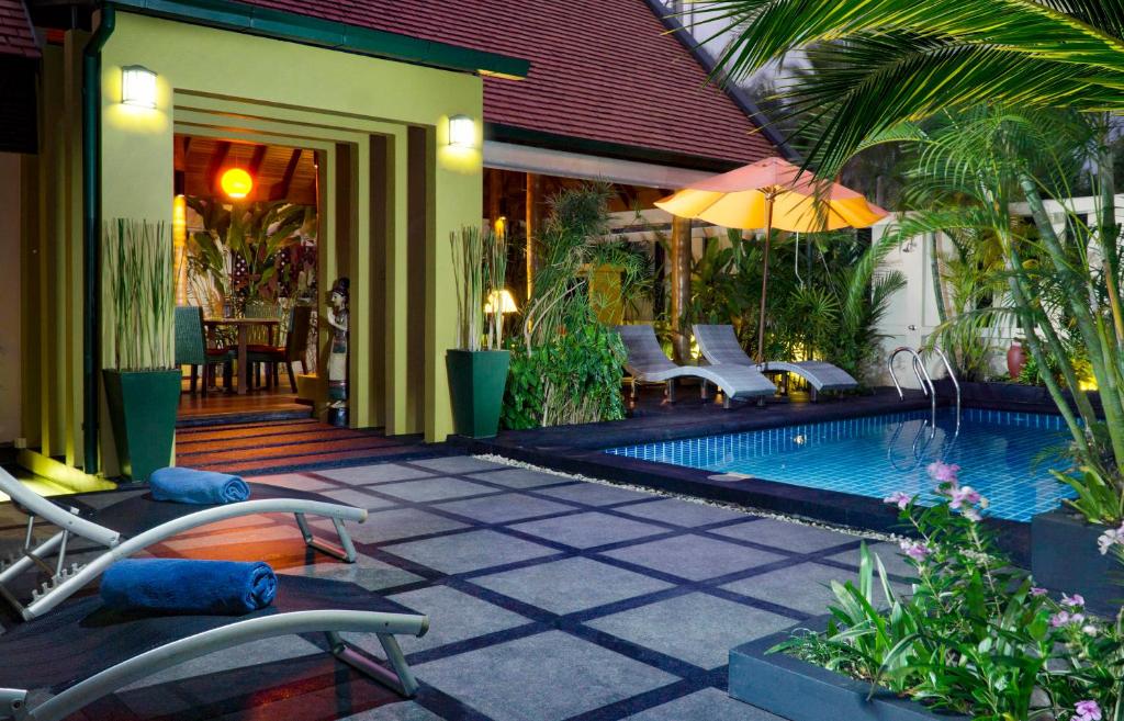a resort with a swimming pool with chairs and an umbrella at Hideaway Villa in Laem Set Beach