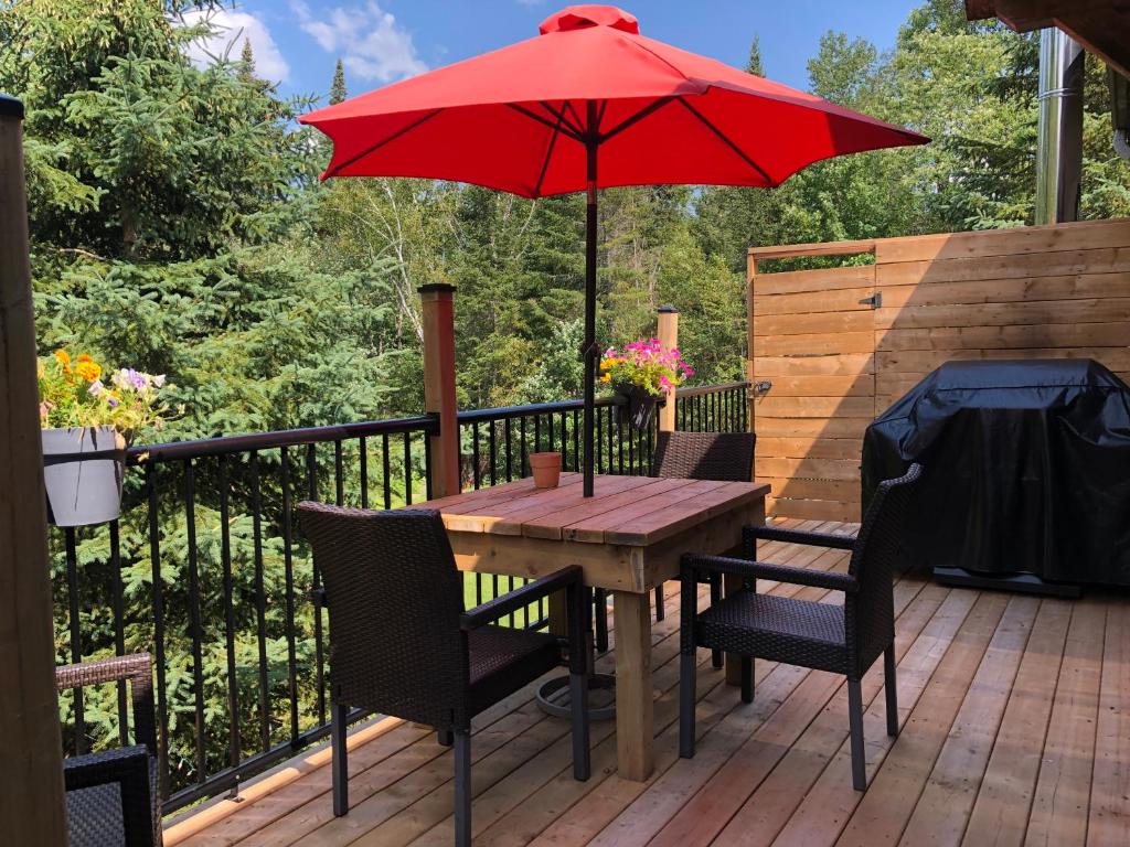 a wooden table and chairs with a red umbrella on a deck at Chalets et Studios Le Vent Du Nord in Lac-Superieur