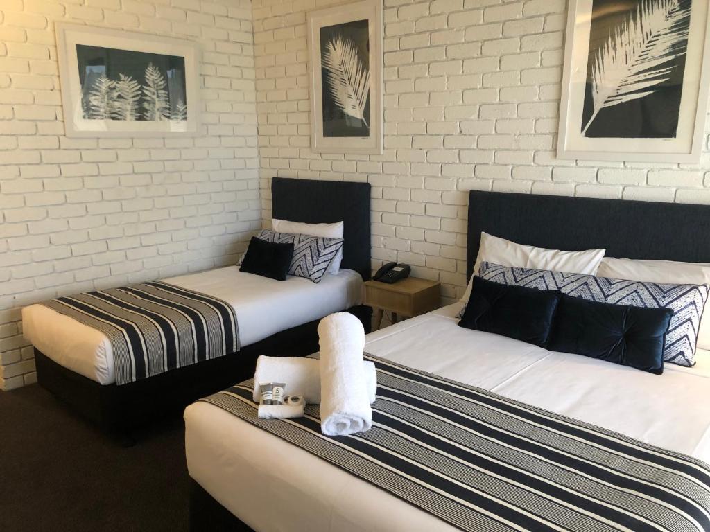 two beds in a hotel room with towels on the beds at Cessnock Vintage Motor Inn in Cessnock