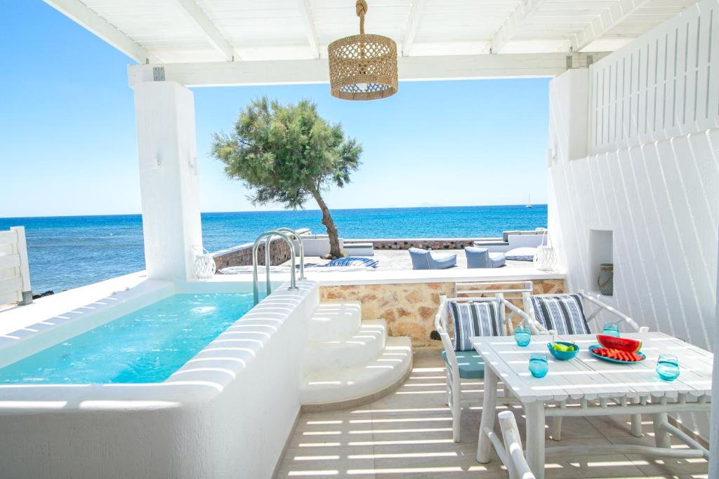 a patio with a tub and tables and the ocean at Aegean Melody Suites in Vlychada