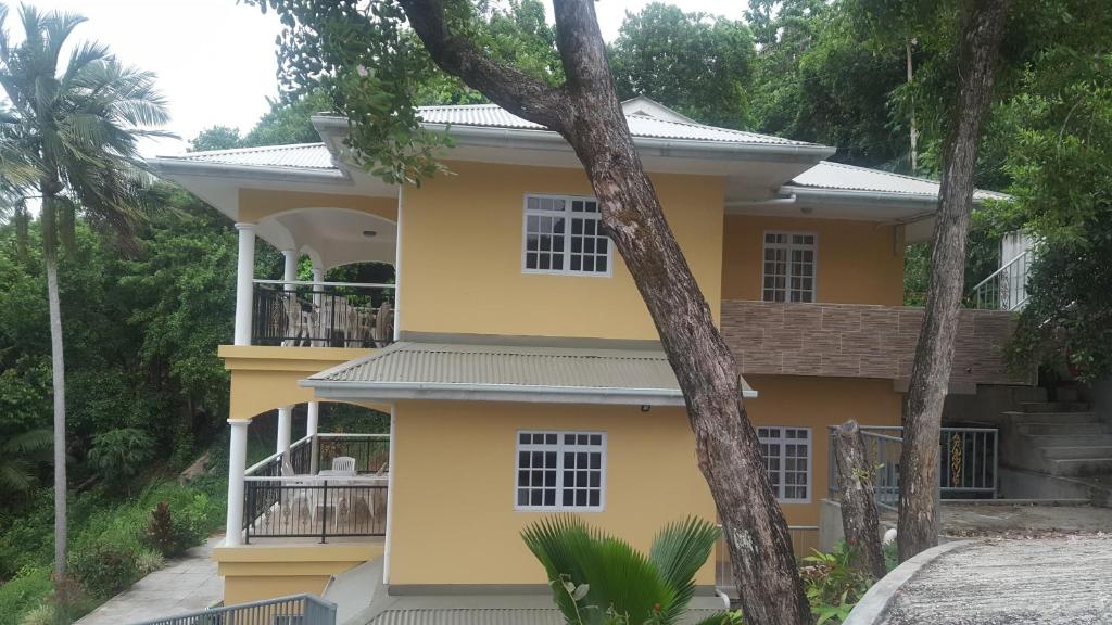 a yellow house with trees in front of it at Anse Royale Bay View Apartments in Mahe