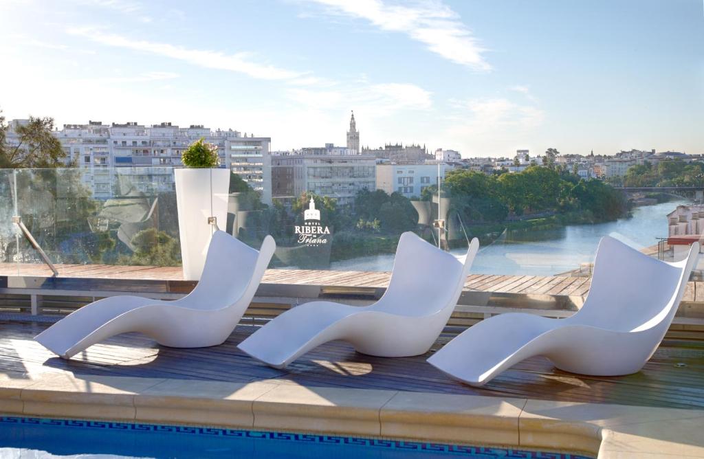 três cadeiras brancas sentadas à beira de uma piscina em Ribera de Triana Hotel em Sevilha