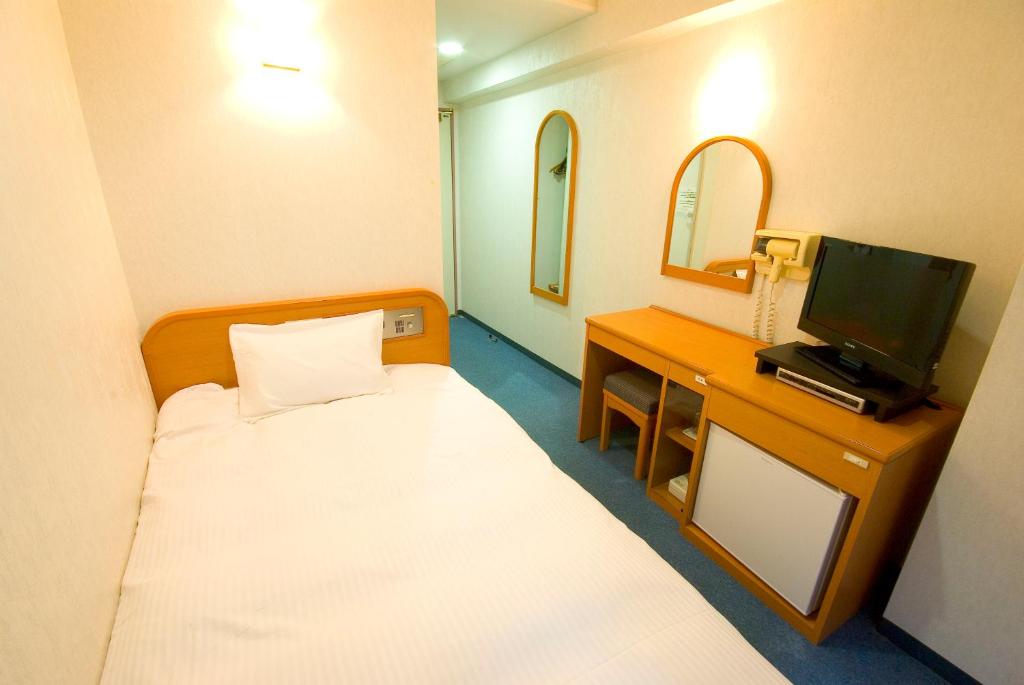 a room with a bed and a desk with a television at GR Hotel Suidocho in Kumamoto
