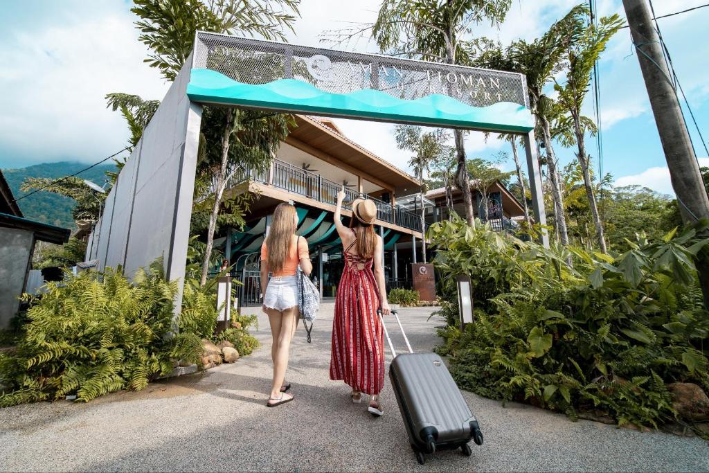 dos mujeres caminando hacia un edificio con una maleta en Aman Tioman Beach Resort, en Tioman Island