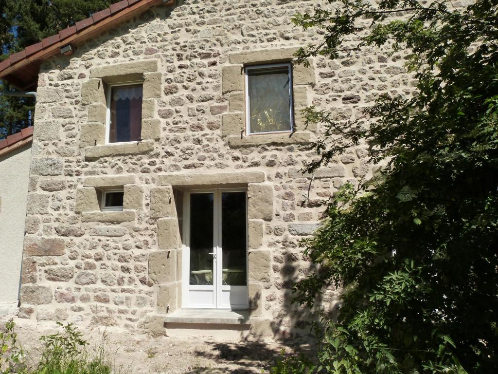 a stone house with a white door and windows at Gîte Le Pont du Monet in Usson-en-Forez
