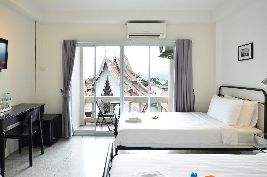 a hotel room with two beds and a desk and a window at Fav Inn Town in Chiang Mai