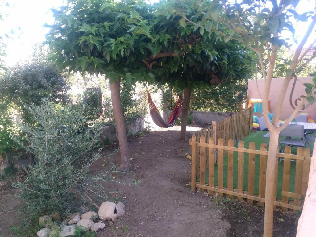 een tuin met een hek en een hangmat onder twee bomen bij Appartement 62 m2 1er etage avec jardin au rdc in Saint-Génis