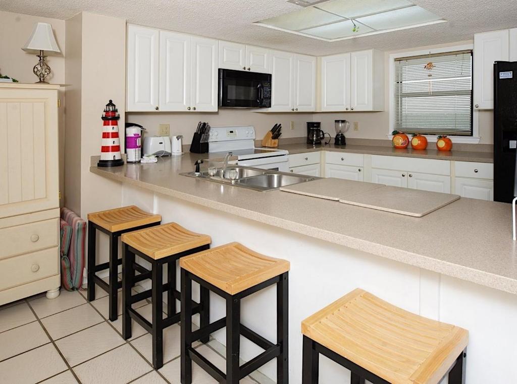 una cocina con armarios blancos y taburetes de bar en Sunswept 807 Condo en Orange Beach