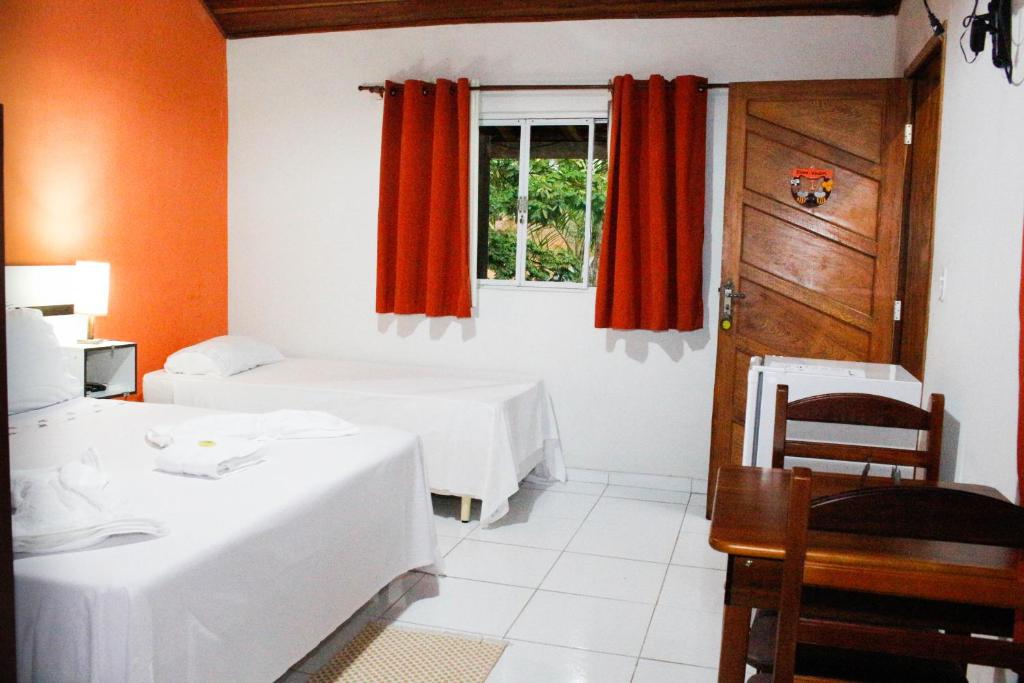 a room with two beds and a window with red curtains at Pousada Doce Mel in Penedo