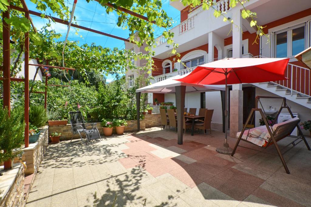 un patio con sombrilla roja, mesa y sillas en Apartments Petra, en Marina