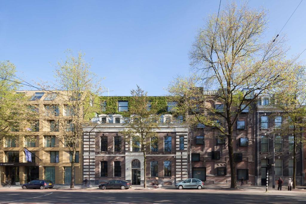 un grand bâtiment en briques avec des voitures garées devant lui dans l'établissement Hyatt Regency Amsterdam, à Amsterdam