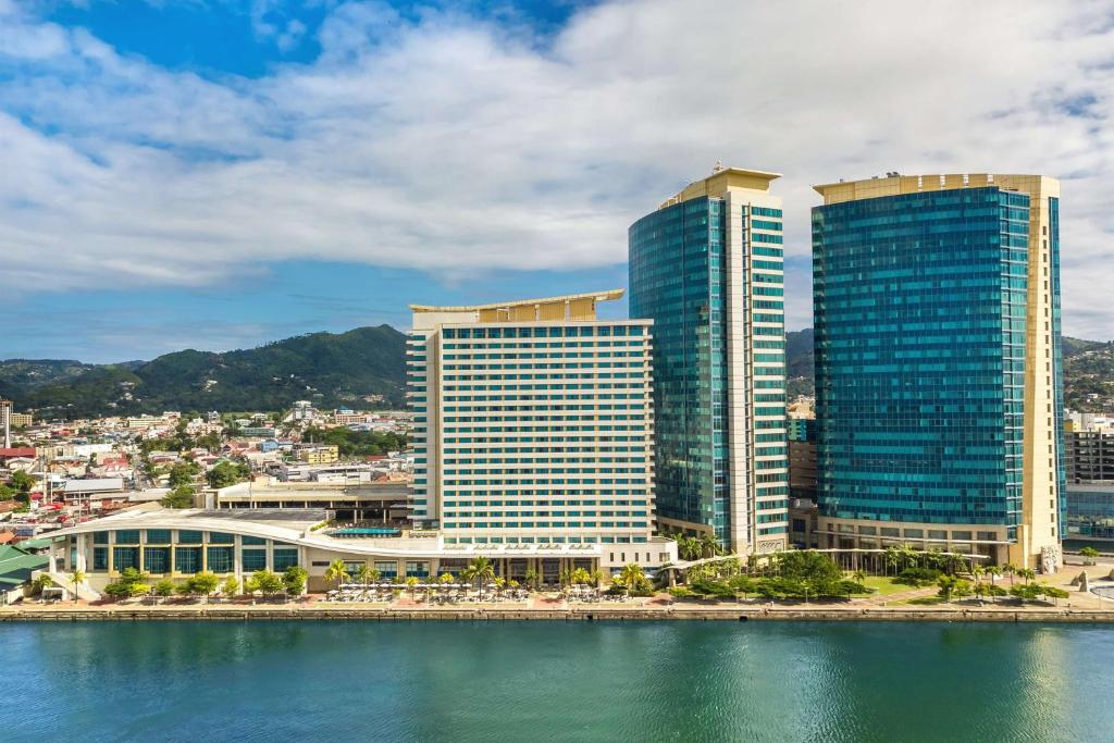 eine Gruppe hoher Gebäude neben einem Wasserkörper in der Unterkunft Hyatt Regency Trinidad in Port of Spain