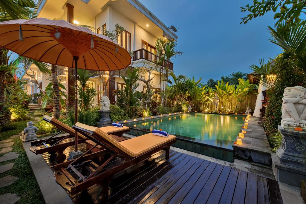 a swimming pool with chairs and an umbrella next to a house at Cenik Villa Ubud in Ubud