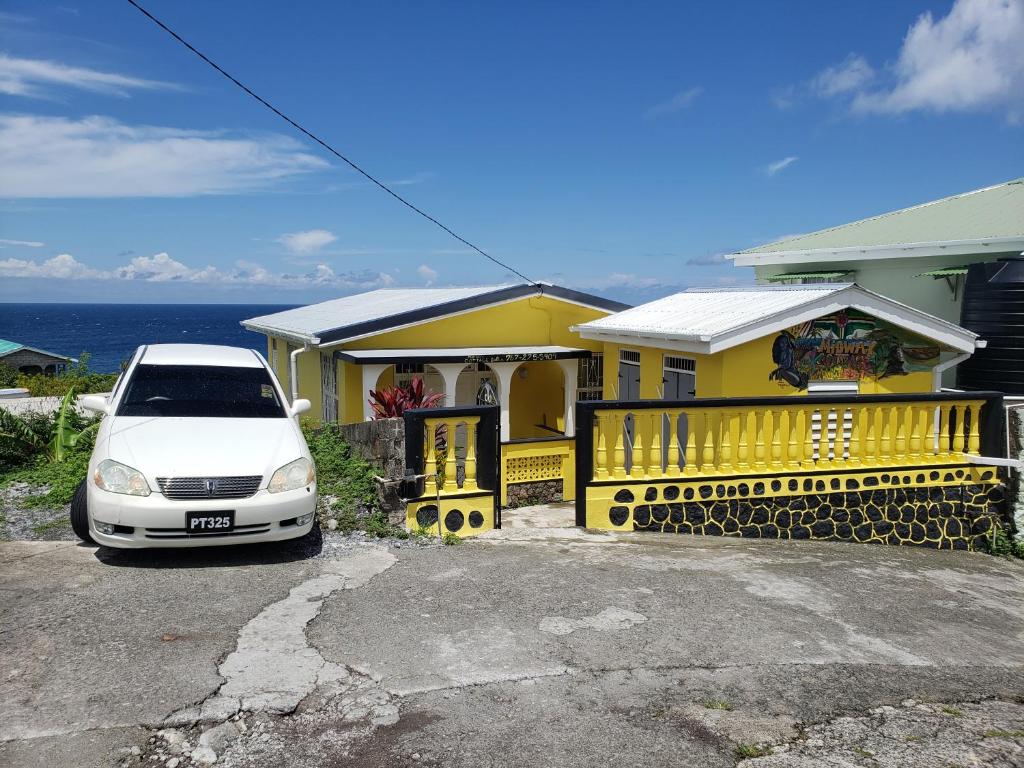 a white car parked in front of a yellow house at Midway Cottage in Scotts Head Village