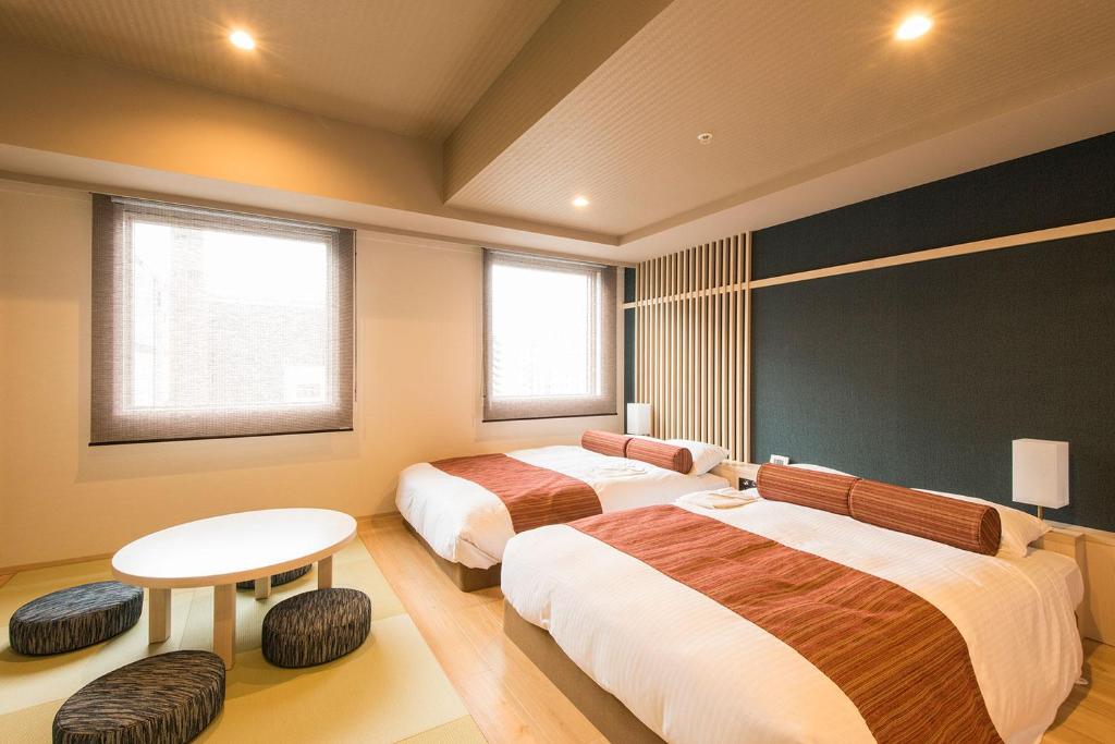 a bedroom with two beds and a table and two windows at Rembrandt Style Sapporo in Sapporo