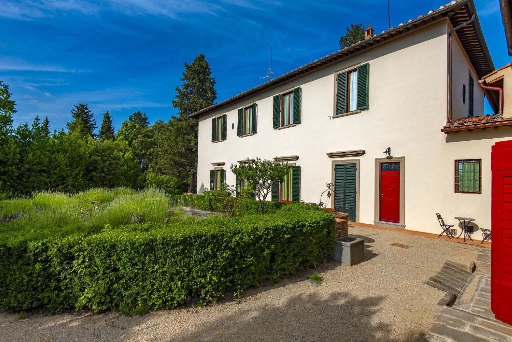 ein weißes Haus mit einer roten Tür und einer Hecke in der Unterkunft Agriturismo Villa Ulivello in Chianti in Strada