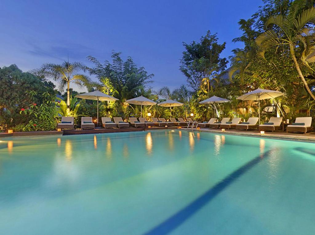 a swimming pool with chairs and umbrellas at a resort at Bali Agung Village - CHSE Certified in Seminyak