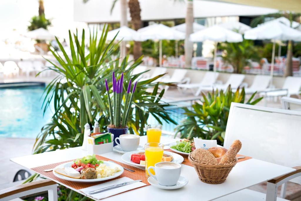 einen Tisch mit Frühstücksspeisen und Getränken neben einem Pool in der Unterkunft Lagoona by Isrotel Collection in Eilat