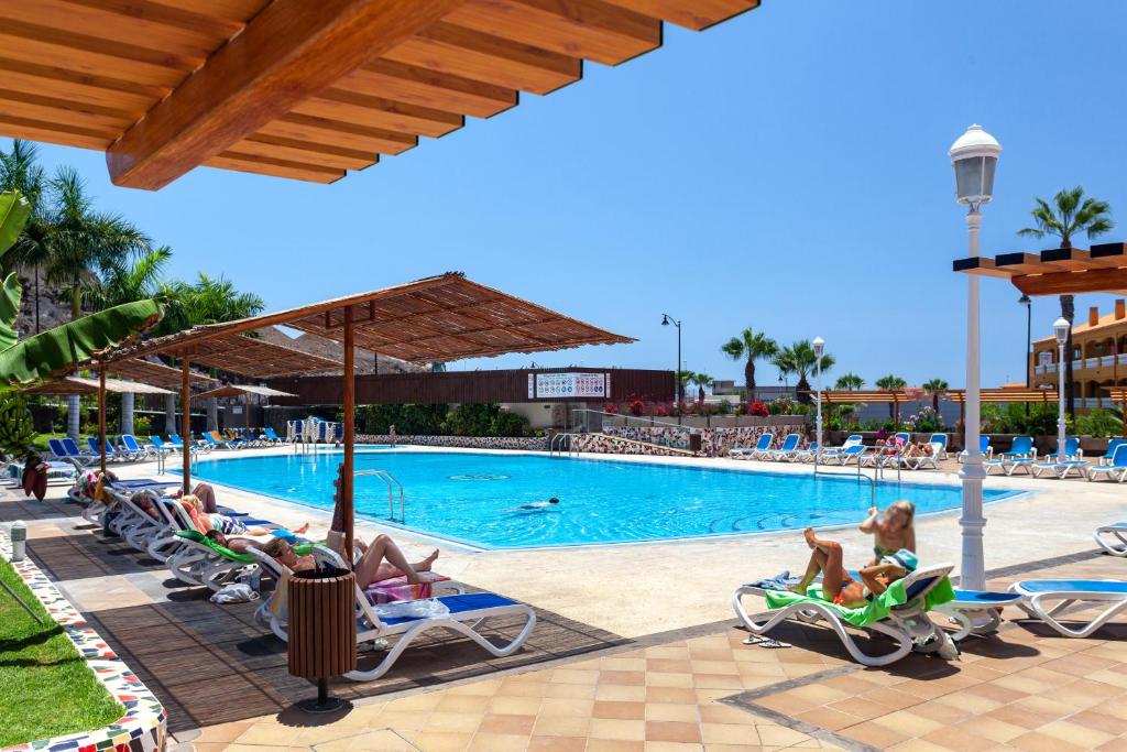 a group of people sitting in lawn chairs by a pool at Apartamento Ocean View in Puerto de Santiago