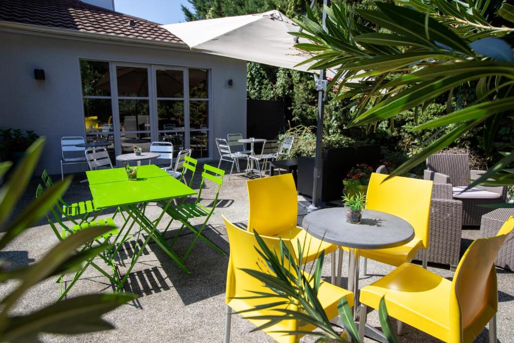 a patio with yellow chairs and tables and an umbrella at Première Classe Lyon Sud - Pierre Bénite in Irigny