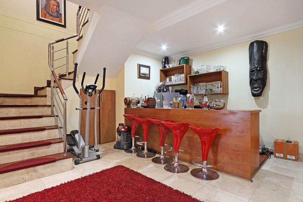 a room with a bar with red chairs and stairs at Natalie Guesthouse in Bloubergstrand